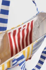 Bolso tipo tote de gran capacidad, confeccionado en algodón con diseño patchwork de rayas verticales y horizontales en colores amarillo, rojo, azul y blanco. Incluye un bolsillo frontal con un parche bordado con el escudo nacional.