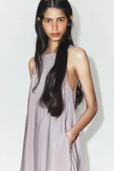 Vestido midi de corte fluido y diseño minimalista, con cuello redondo y mangas sisa. Presenta una abertura en la espalda con cierre y lazada ajustable.