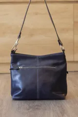 Cartera de cuero color beige, de diseño estructurado, con bolsillo frontal con cierre y detalles en cuero grabado con efecto reptil. Cuenta con correa ajustable para llevar al hombro o cruzada.