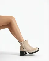 Bota corta de cuero en tono beige, con diseño bicolor que presenta un panel lateral en un tono más claro. Cuenta con un taco cuadrado negro de altura media y cierre lateral interno.