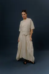 Blusa de lino color crudo, con cuello mao, mangas cortas y cierre frontal cruzado con nudos de tela y botones.