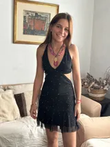 Vestido corto negro con estampado de plumas doradas, escote en V, breteles finos cruzados en la espalda, cut-outs laterales y volado en el ruedo.