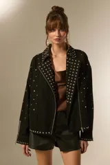 Campera de jean negra con tachas plateadas en el cuello, solapas y parte delantera. Tiene cierre asimétrico, bolsillos laterales con cierre y puños con cierre.