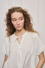 Camisa de manga corta color celeste, confeccionada en viscosa fluida, con silueta amplia y escote redondo con frunces y lazo para anudar.