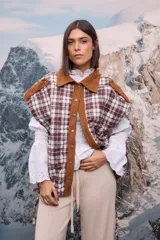 Chaleco acolchado con diseño a cuadros en tonos marrones y blancos, con cuello y solapa frontal en pana marrón. Presenta cierre con botones metálicos y detalles de costura en los hombros.