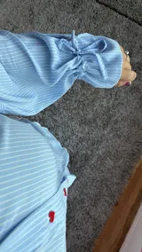 Camisa oversize de fibrana a rayas celestes y blancas, con cuello clásico, mangas largas con puños y botones frontales de acrílico en forma de corazón rojo.