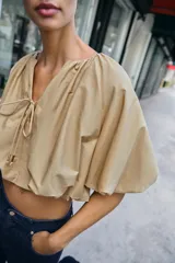 Cuerpo corto de cuello redondo con frunces, escote en pico con lazada y mangas cortas abullonadas con elástico interior.