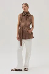 Chaleco largo marrón de algodón con cuello camisero, cierre frontal con botones, bolsillos laterales y lazo ajustable en la cintura.