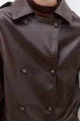 Trench corto color chocolate de cuero sintético, con doble botonadura, cuello alto y charreteras en los hombros.