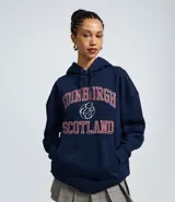 Buzo tipo canguro de corte oversized, color azul marino, con capucha ajustable y bolsillo frontal. Presenta un estampado estilo college en el pecho con la inscripción 'Edinburgh Scotland' en letras rojas y blancas.