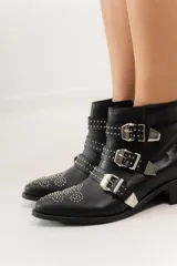 Botas cortas de cuero negro con puntera fina, taco bajo y cierre lateral. Presentan tres correas con hebillas plateadas y apliques de tachas plateadas.