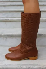Bota de caña alta confeccionada en cuero, con diseño de textura perforada en la parte superior de la caña y puntera lisa. Cuenta con suela plana y taco bajo.
