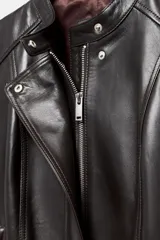 Chaqueta de cuero de corte entallado con cuello subido, cierre frontal con cremallera y botones ocultos bajo solapa. Presenta bolsillos delanteros con cierre y mangas largas terminadas en cremalleras metálicas.