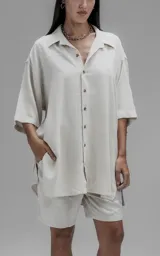 Camisa de corte oversize con cuello camisero, cierre frontal de botones y mangas cortas. Presenta un diseño holgado con bolsillos laterales integrados en la costura.