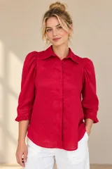 Camisa de lino color blanca, con cuello clásico, mangas tres cuartos abullonadas en los hombros y terminación con volados en los puños, cierre frontal con botones ocultos.