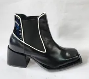 Bota tipo chelsea de cuero negro con detalles de costuras en blanco, puntera cuadrada y taco bloque.