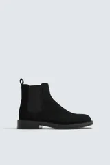 Bota estilo Chelsea de hombre, fabricada en piel con acabado de serraje. Presenta elásticos laterales, horma redonda y suela con ligero tacón.