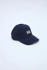 Gorra de pana azul marino con visera curva, parche frontal con texto y pequeño bordado rojo en el lateral.