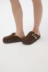 Suecos negros de estilo zueco con capellada de cuero sintético, detalle de hebilla metálica dorada y tachas decorativas alrededor de la suela. Poseen plantilla ergonómica y suela de plataforma dentada.