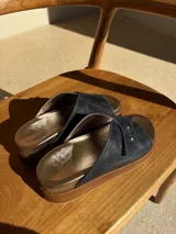 Sandalia de cuero con diseño de tiras cruzadas en color azul oscuro, detalle de doble remache dorado y plataforma de madera con plantilla metalizada.
