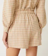 Short tipo clochard de tiro alto confeccionado en tejido tweed con estampado cuadrillé en tonos beige y crema. Presenta cintura elástica, bolsillos laterales y detalle de botones metalizados frontales.