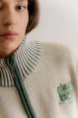 Saco tejido tipo jacquard color bordó con diseño floral en la espalda, cuello alto y cierre frontal de aluminio. Presenta detalles en azul y blanco en el cuello, puños y ruedo, con un patrón geométrico de rombos en la parte inferior.