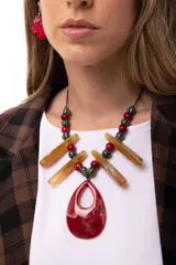 Collar con dije central en forma de gota de resina roja marmolada, acompañado de bastones de resina color ámbar y cuentas esféricas de cerámica en tonos rojo y verde petróleo. Se sujeta mediante un cordón ajustable.