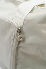 Bolso de viaje tipo duffle, color beige, confeccionado en material sintético ligero. Cuenta con doble asa de mano, cierre principal superior, bolsillo frontal con cierre y compartimento inferior independiente con cierre.