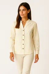 Camisa de manga larga color crema, con cuello mao y apliques bordados de hojas y flores en tono similar. Cierre frontal con botones marrones.