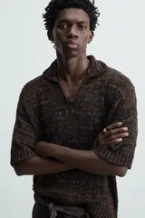 Polo de punto de calce relajado, color marrón oscuro jaspeado con negro. Presenta cuello solapa con abertura frontal en V y mangas cortas.