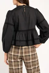 Blusa negra de algodón con diseño de broderie y calados en el pecho y hombros. Presenta corte oversize, mangas largas con puños y un detalle de volado en la cintura.