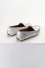 Mocasines plateados de cuero con cordones decorativos y suela de goma marrón.