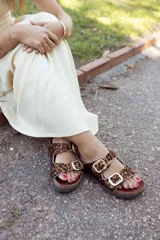 Sandalias bajas con estampado de leopardo, dos tiras con hebillas doradas ajustables y suela plana.