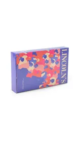 Billetera mediana de cuero sintético con diseño bicolor en naranja y fucsia. Cuenta con cierre perimetral, correa de muñeca extraíble y placa metálica decorativa con logo.