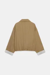 Chaqueta corta de color verde militar, con cuello solapa, bolsillos delanteros con solapa y cierre frontal de botones ocultos. Presenta mangas amplias con vuelta en los puños que muestran un forro a rayas.