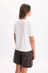 Camiseta blanca de manga corta con estampa frontal en color bordó y verde con la leyenda 'The Sunday Club' y texto descriptivo.