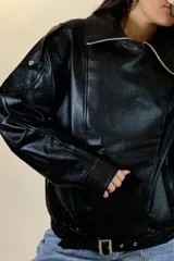 Chaqueta de ecocuero negro con diseño oversize, cuello solapa, cierre frontal y cinturón ajustable en el ruedo.