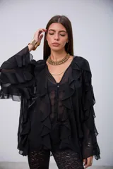 Blusa de tela semitransparente color negro, con diseño de volados verticales a lo largo del frente y en las mangas. Presenta cierre frontal con botones y cuello en V.