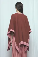 Poncho marrón con detalles de bordes ondulados en color rosado, confeccionado en mezcla de acrílico, poliéster y elastano, de diseño abierto y mangas amplias.