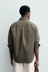 Camisa de corte relajado confeccionada en una mezcla de lyocell y algodón con efecto lavado. Presenta cuello solapa, manga larga con puños abotonados, bolsillo de plastrón en el pecho y cierre frontal con botones.