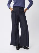 Pantalon de corte sastrero y pierna ancha, confeccionado en denim azul oscuro. Presenta costuras verticales frontales que simulan un tableado, cintura con trabillas y bolsillos laterales.