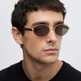 Lentes de sol con montura ovalada de acero inoxidable en color dorado y cristales polarizados en tono marrón. Presentan un diseño de puente fino y patillas con terminación en carey.