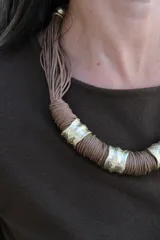 Collar de diseño artesanal compuesto por múltiples hilos de cuero color chocolate, adornado con piezas cilíndricas de metal dorado con textura irregular.