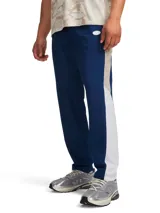 Pantalón deportivo Under Armour modelo Rival Woven CB Pants, de corte recto en color azul marino con franjas laterales en color beige y blanco, cintura elástica y tecnología UA Storm repelente al agua.