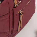 Cartera tipo bolso de color bordó, confeccionada en material textil con detalles en cuero sintético color suela. Cuenta con doble asa de mano, un bolsillo frontal con cierre y tiradores decorativos, además de una correa larga ajustable y extraíble.