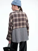 Camisa de corte relajado con diseño combinado. La parte superior presenta un estampado a cuadros en tonos marrones y negros, mientras que la parte inferior destaca por un panel de rayas verticales en color bordó. Cuenta con cierre frontal de botones y mangas largas.