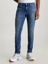 Jeans de hombre, talle bajo, corte slim ajustado, confeccionados en denim azul medio vintage con efecto desgastado. Presentan bragueta con cremallera y diseño de cinco bolsillos.