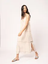 Vestido largo color crudo de lino, con silueta recta, escote en V, breteles anchos, detalle de elástico en la espalda y tajos laterales.