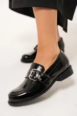 Mocasines negros de charol arrugado con horma redondeada y detalle de presilla con hebilla y ojalillos.