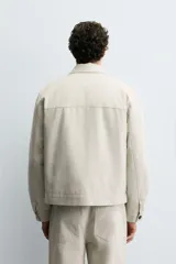 Sobrecamisa de corte regular confeccionada en tejido con estructura canvas color marrón. Presenta un ligero acolchado interior, cuello de solapa y cierre frontal con cremallera metálica. Incluye dos bolsillos de plastrón en el pecho y bolsillos laterales de vivo, con mangas largas terminadas en puños con botón.